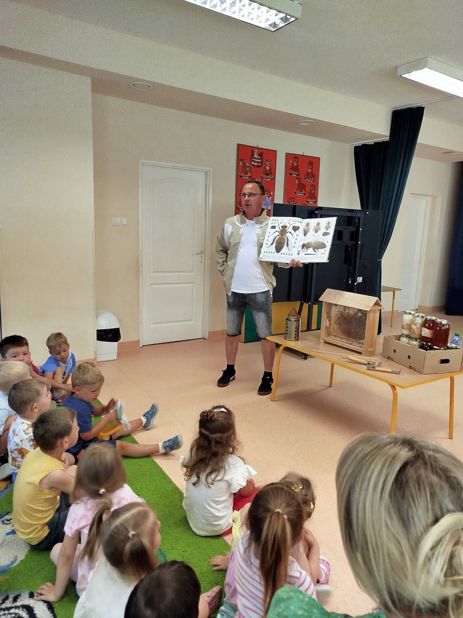 Pszczelarz prezentuje dzieciom planszę o pszczołach i wyposażenie pasieki